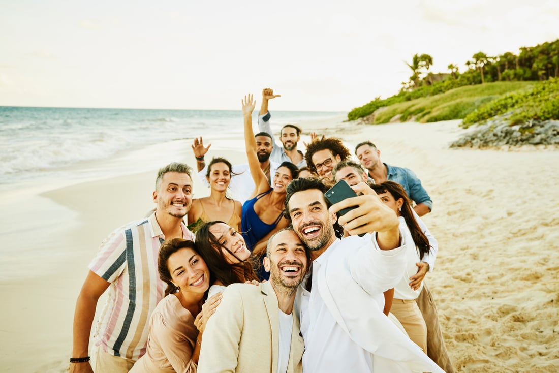 Wide shot of smiling gay couple taking selfie with friends and  after wedding ceremony on tropical beach